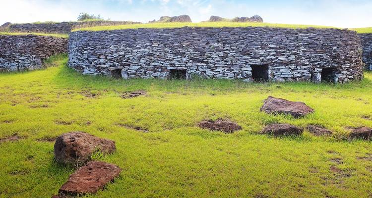 Casas de piedra circulares antiguas con pequeñas puertas ubicadas en un campo cubierto de pasto en la Isla de Pascua.