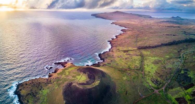 Una impresionante vista aérea de la accidentada costa de la Isla de Pascua y su cráter volcánico encontrándose con el océano al amanecer.