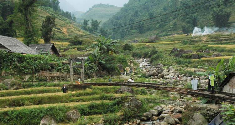 Bridge crossing a rocky stream in a lush, mountainous area.