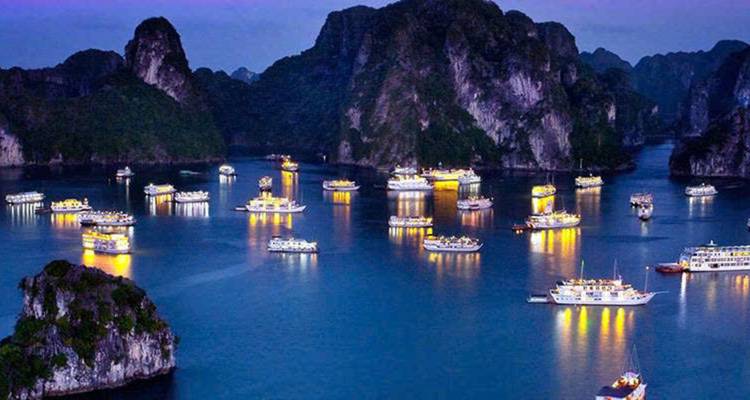 Boats illuminated at night in a bay surrounded by limestone formations.