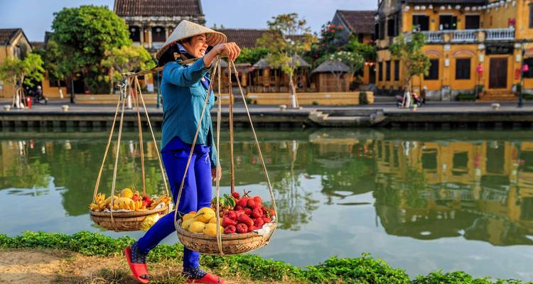 Frau, die Körbe mit Obst neben einem Kanal in einer charmanten Stadt trägt.