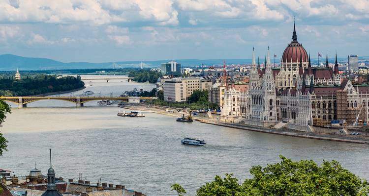 Panoramablick auf das Parlamentsgebäude von Budapest und die Donau mit Brücken und Booten an einem dunstig-schwülen Sommertag.