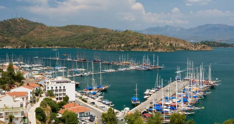 Marina de Fethiye avec des rangées de goulettes amarrées le long d'une longue jetée et des collines boisées au-delà
