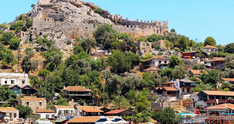 Stone fortress crowned hilltop village with terracotta roofs and lush vegetation
