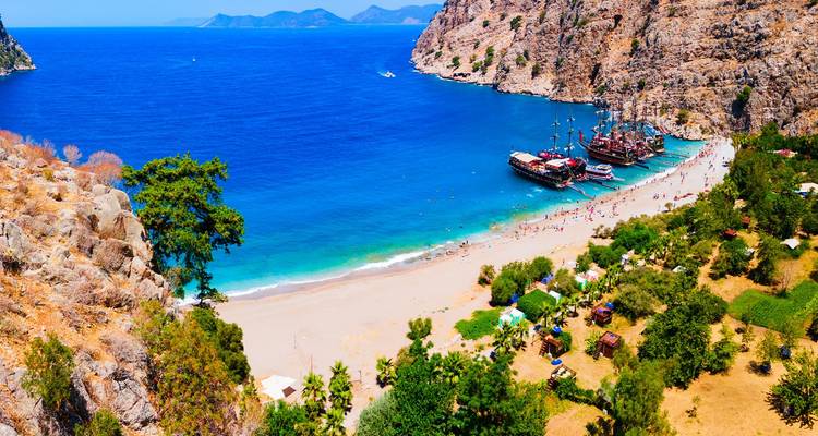 Vibrant sandy beach in a sheltered cove with anchored excursion boats and sunbathers