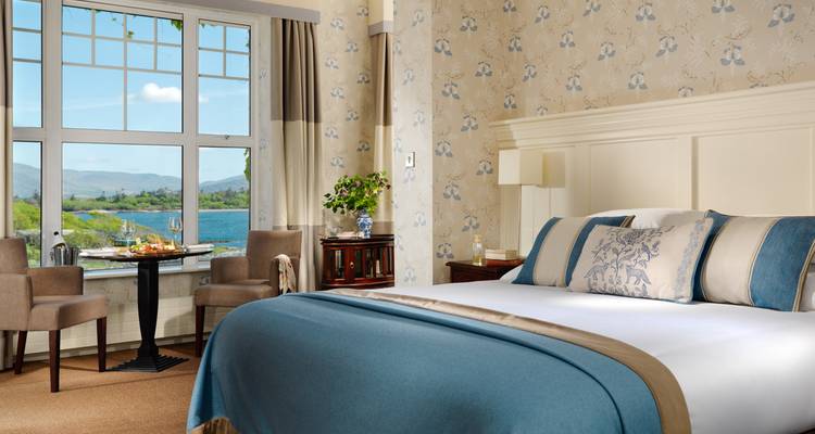 Elegantes Hotelzimmer mit Seeblick durch großes Fenster und sanfter blauer Einrichtung.