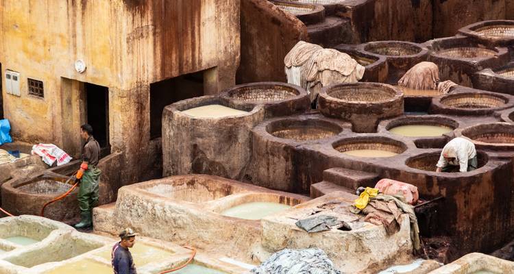 Werkers in een traditionele leerlooierij met stenen bakken vol kleurrijke verfstoffen.