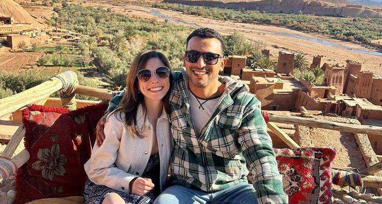 Een stel dat zit op een terras met een schilderachtig uitzicht op een woestijnlandschap en woningen beneden.