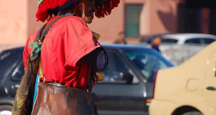 Een verkoper in traditionele kleding in een stedelijke omgeving met auto's op de achtergrond.