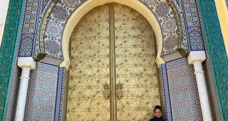 Persoon die voor een grote, sierlijke, gouden en blauwe deur staat in een historische omgeving.