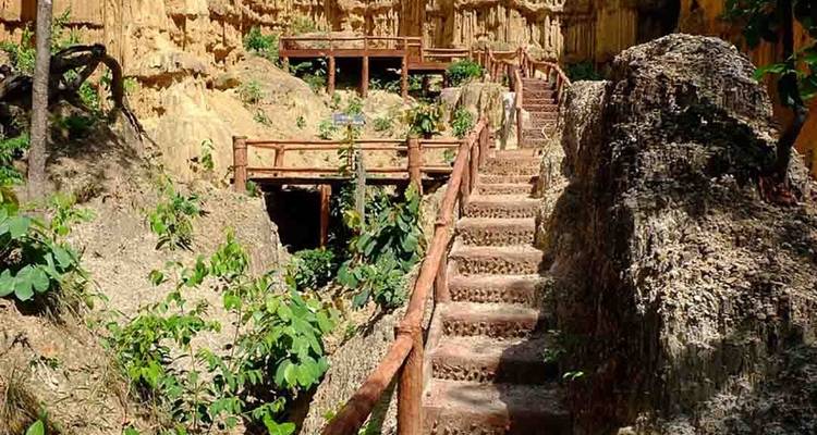 Wooden stairs and walkways wind through eroded sandstone cliffs and lush vegetation in a canyon setting.