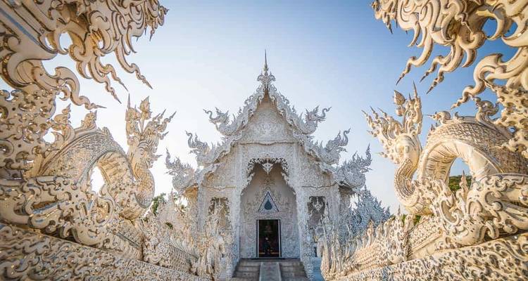 The ornate white facade of Wat Rong Khun gleams under a clear blue sky.