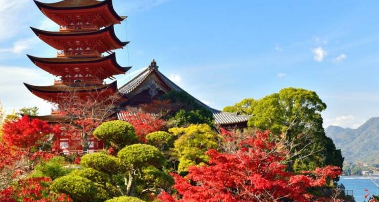 Pagoda roja de cinco pisos rodeada de vibrante follaje otoñal con vistas al mar en Miyajima.