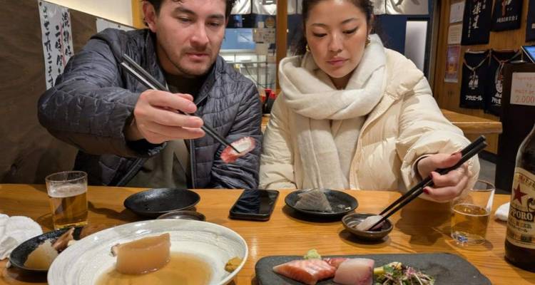 Dos comensales usan palillos para probar sashimi variado y platos japoneses en una acogedora mesa de restaurante.