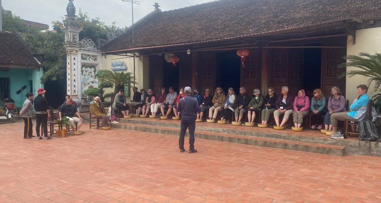 Eine Gruppe von Menschen, die vor einem traditionellen vietnamesischen Gebäude sitzen.