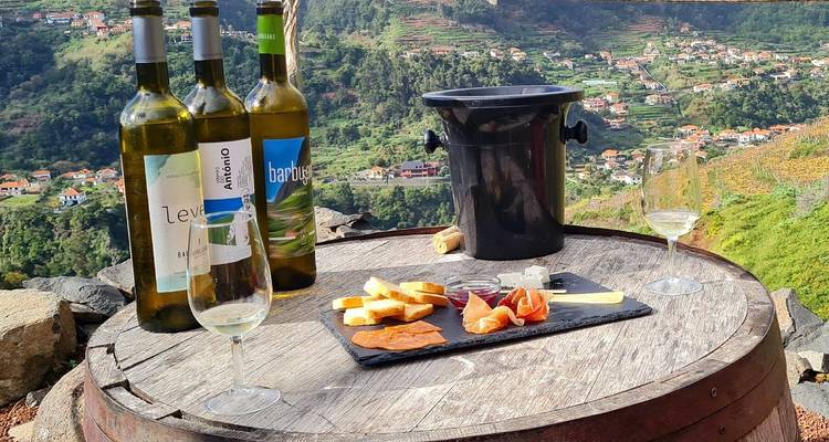 Wine bottles, glasses and local tapas arranged on a barrel overlooking lush Madeiran valley