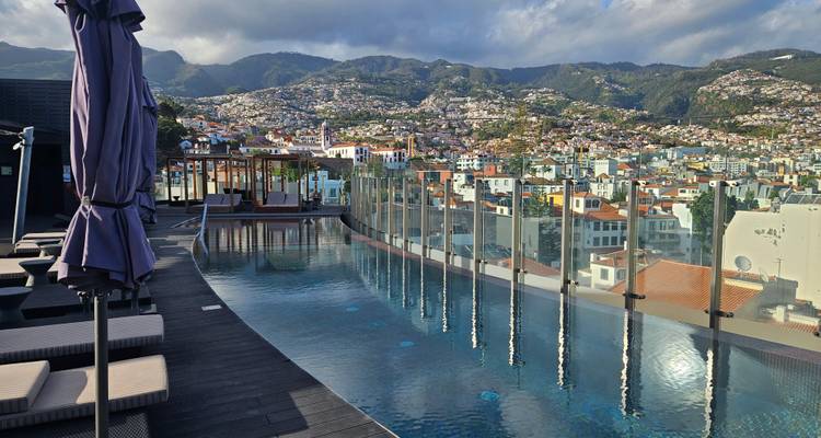 Infinity rooftop pool with glass panels overlooking the cityscape and surrounding green mountains