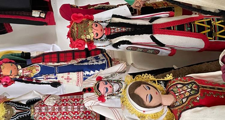 Colorful handcrafted dolls wearing traditional Balkan folk costumes displayed on shelves.