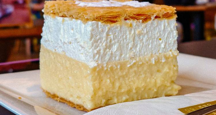 Tranche carrée généreuse de gâteau à la crème pâtissière avec des couches de pâte feuilletée croustillante et une légère poudre de sucre, servie sur une assiette.