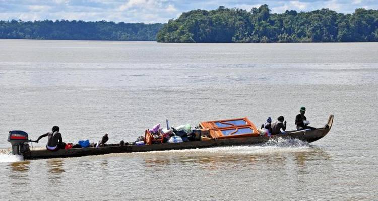 A boat with people and goods on a river with lush greenery in the background.