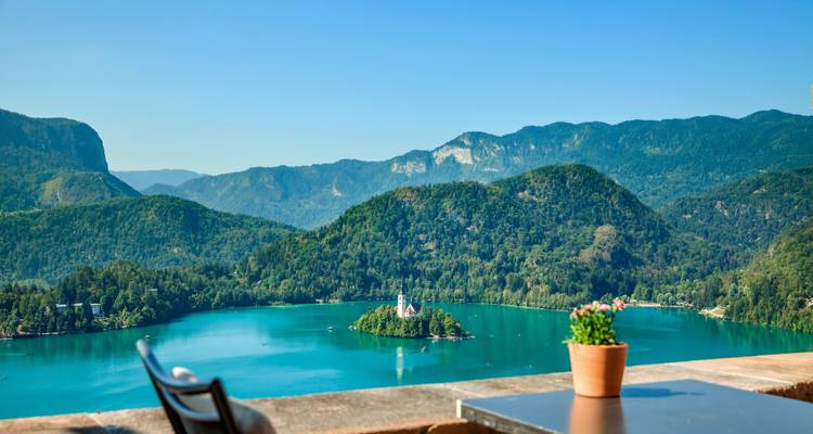 Een sereen uitzicht op een meer met een klein eiland met een kerk en bergen op de achtergrond.