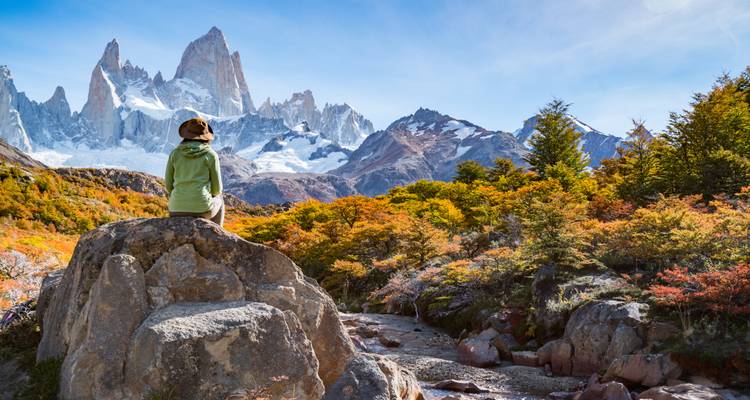 Persoon zittend op een rots met uitzicht op herfstige landschappen en bergen.