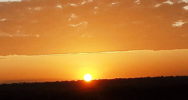 Ein lebhafter oranger Sonnenuntergang über einer silhouettierten Landschaft mit vereinzelten Wolken.