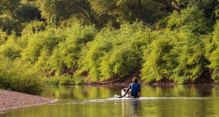 Personne pagayant en canoë sur une rivière bordée d'une végétation luxuriante.