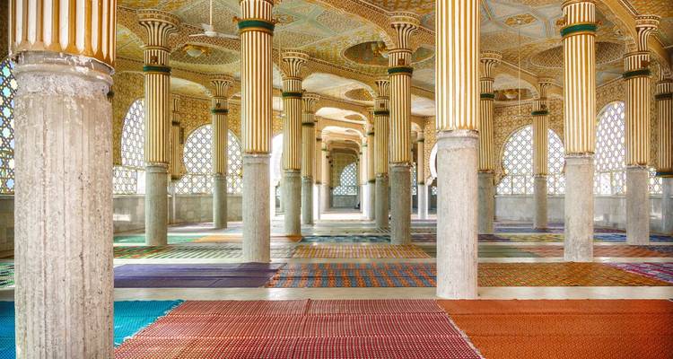 Vue intérieure d'une mosquée avec des colonnes ornées et des tapis.