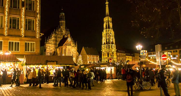 Festive Christmas market at night with illuminated medieval church and ornate fountain tower.