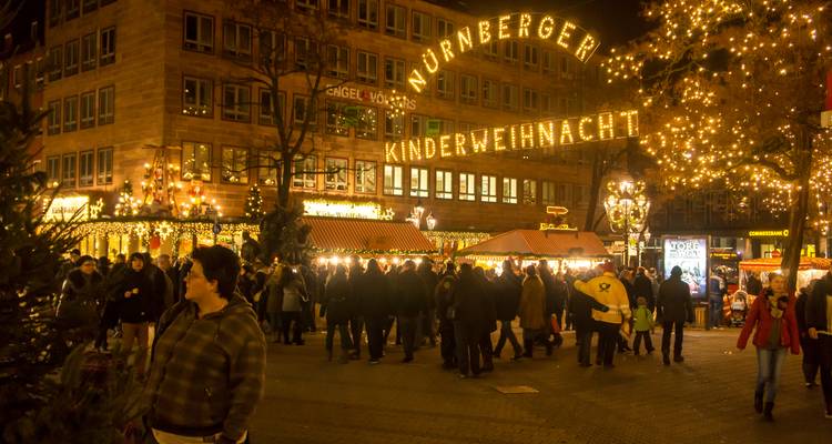 Crowds enjoying an illuminated children’s Christmas market in a city square.