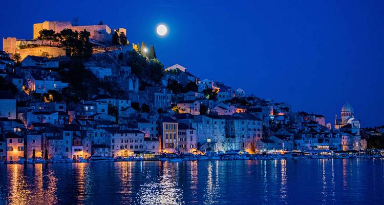 A moonlit waterfront scene with historic buildings.