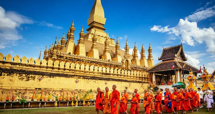 Mönche, die in einer Reihe vor einem goldenen Tempel gehen.