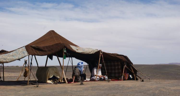 A nomadic tent set up in a desert landscape, two people sitting outside.