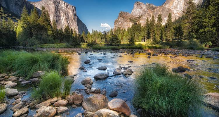 Crystal-clear Merced River flows through Yosemite Valley with granite walls towering above.