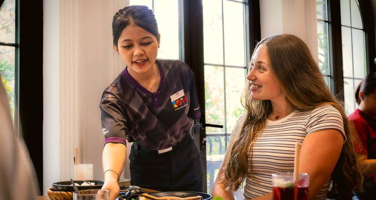 Serveerster demonstreert lokale keuken terwijl een reiziger glimlacht in een fel verlicht restaurant