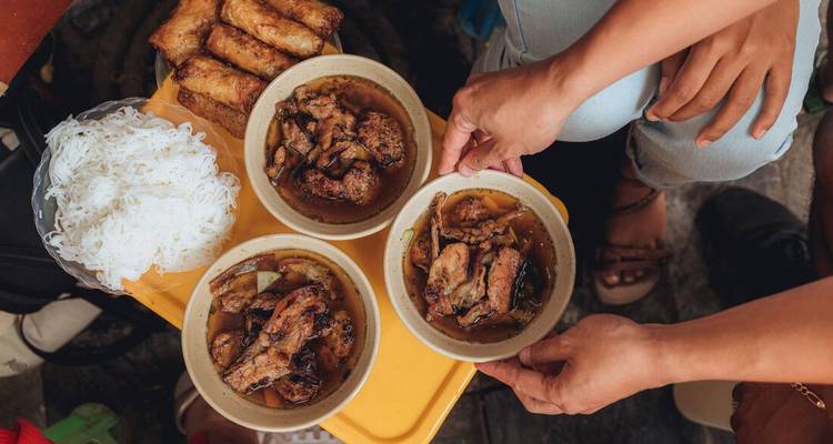 Handen delen schaaltjes Vietnamese bun cha met gegrilde varkensvlees, noedels en verse kruiden