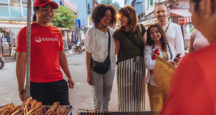 Groep reizigers glimlachen terwijl zij spiesjes uitkiezen bij een levendige straatvoedselkraam