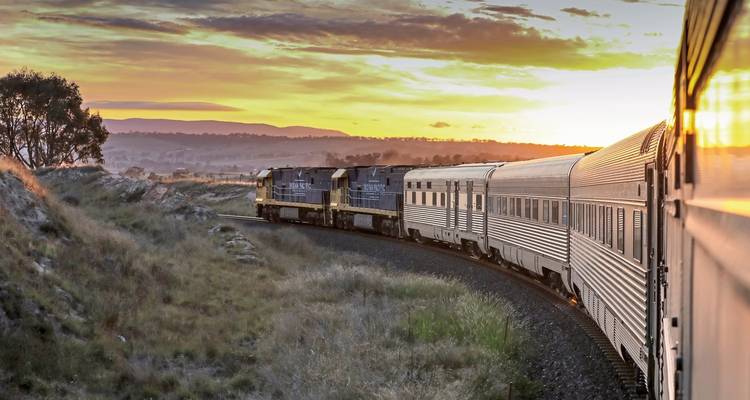 Dramatisch uitzicht van een trein die door schilderachtige landschappen reist bij zonsondergang.