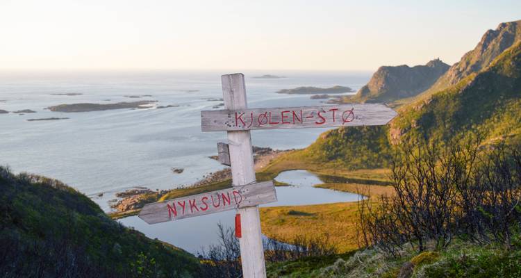 Señal de madera en el sendero señalando hacia Kjølen y Nyksund con un amplio paisaje costero de fondo.