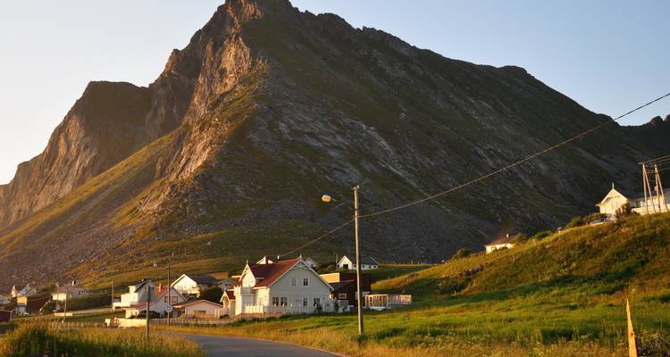 Grupo de casas costeras al pie de una montaña empinada iluminada por el sol en la suave luz del atardecer.