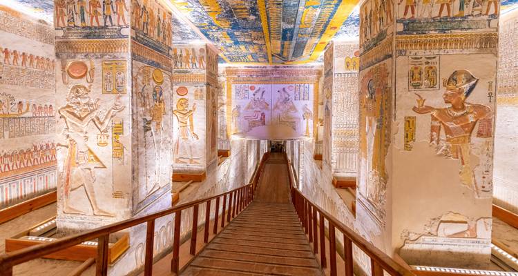 Colorful, well-preserved corridor of an ancient Egyptian tomb with painted pillars and wooden staircase descending.