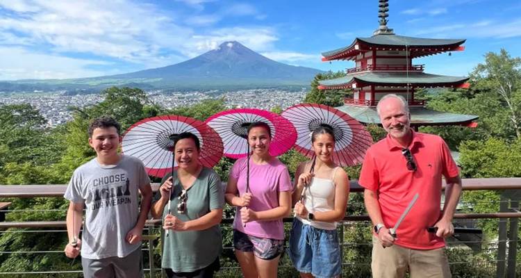 Gruppe von Menschen mit Sonnenschirmen vor einem Tempel und dem Berg Fuji.