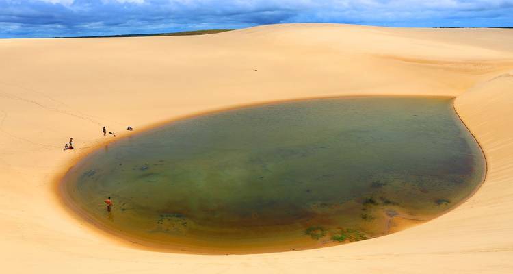 Klare Süßwasserlagune eingebettet in goldenen Sanddünen von Lençóis Maranhenses mit wattenden Besuchern.