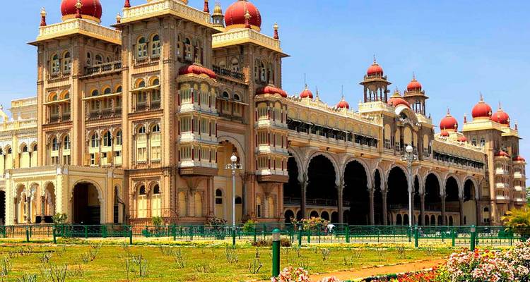 The ornate Mysore Palace with red domes and arches rises above expansive lawns.