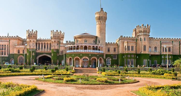 The grand ivy-clad facade of Bangalore Palace with formal gardens and bright blue sky.