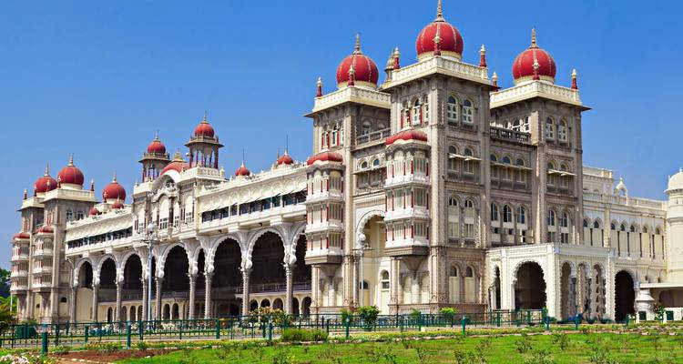 Ornate Mysore Palace with red domes and arched verandas gleaming against a bright blue sky.