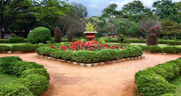 Manicured garden with symmetrical hedges, topiary and red flower bed centred around a large urn.
