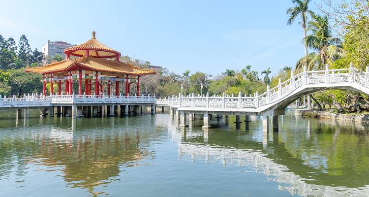 Traditioneller chinesischer Pavillon auf Stelzen über einem ruhigen Parkteich, verbunden durch eine elegante weiße Steinbrücke.