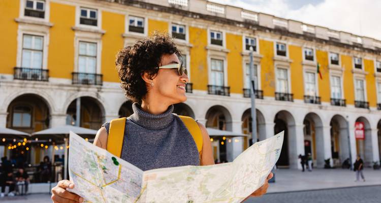Persona sosteniendo un mapa frente a una plaza de edificio amarillo.